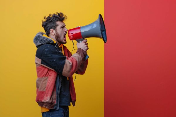 man-with-megaphone-his-hand-is-speaking-front-red-yellow-wall-scaled